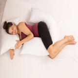 Woman asleep on her side with a white V shaped pillow along her body, one arm behind her back and her top leg over the other